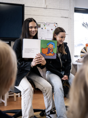 Twee studenten PW laten voorleesboekje zien aan de kinderen